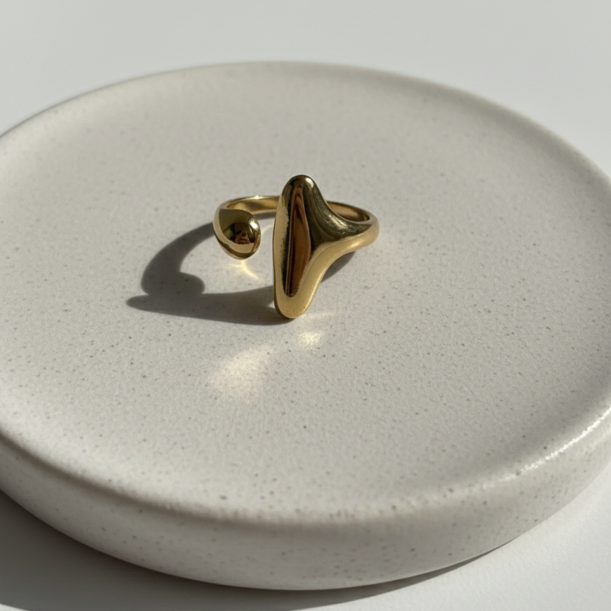 Abstract gold statement ring with elongated molten shape on white background.
