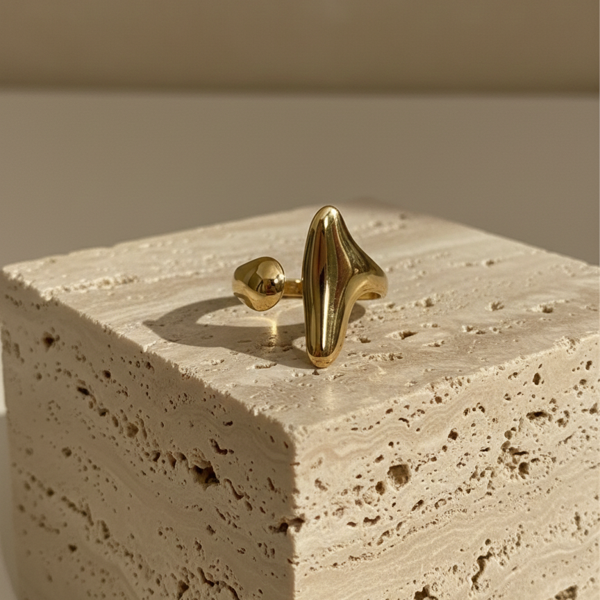 Abstract gold statement ring with elongated molten shape on white background.