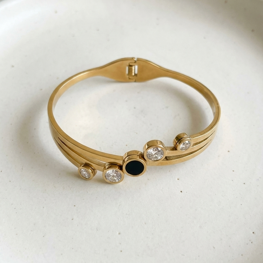 Gold hinged bangle bracelet with black stone and crystal circles on white stand.