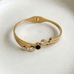 Gold hinged bangle bracelet with black stone and crystal circles on white stand.