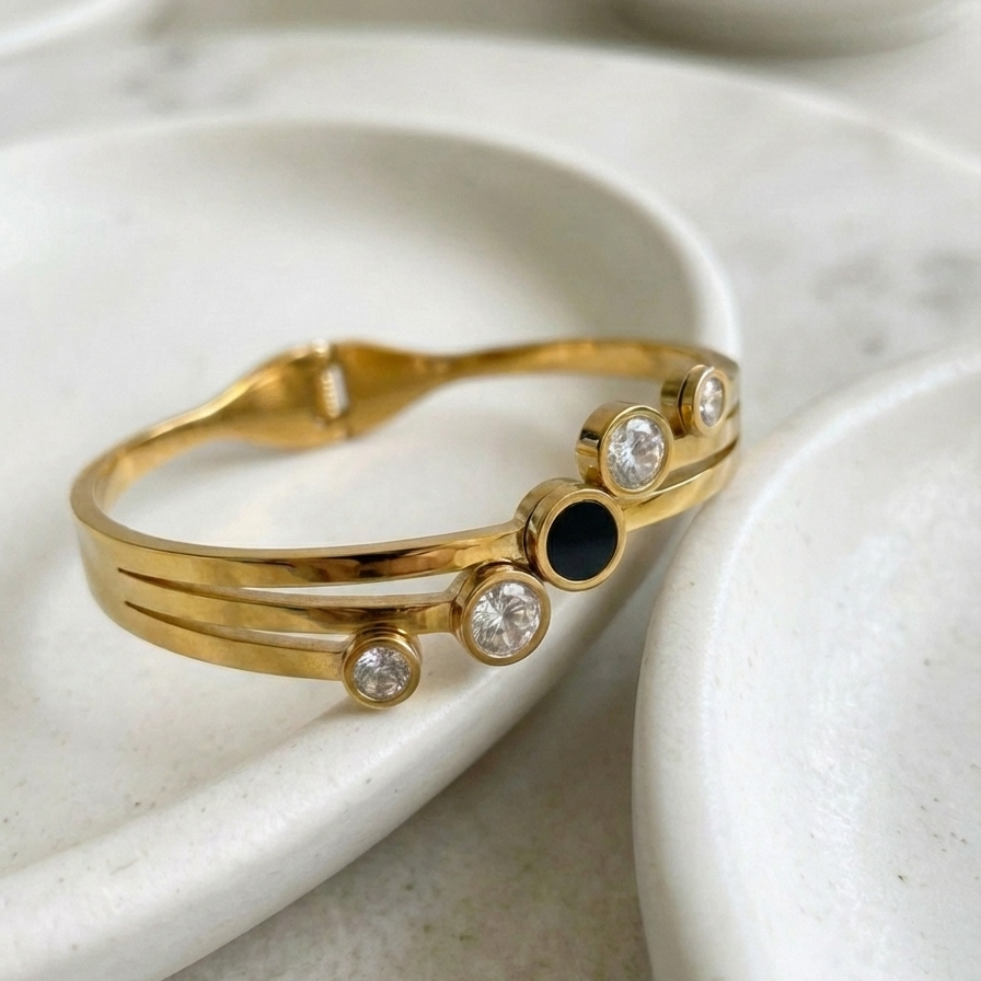 Gold hinged bangle bracelet with black stone and crystal circles on white stand.