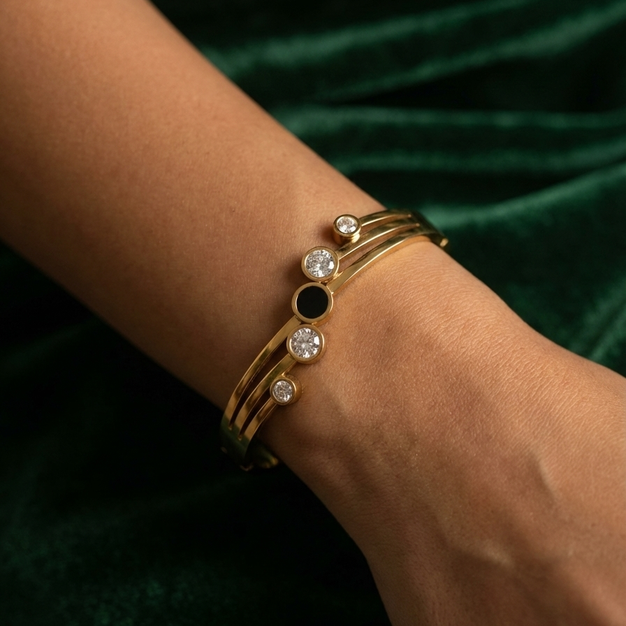 Gold hinged bangle bracelet with black stone and crystal circles on white stand.