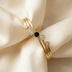 Gold hinged bangle bracelet with black stone and crystal circles on white stand.