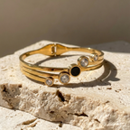 Gold hinged bangle bracelet with black stone and crystal circles on white stand.