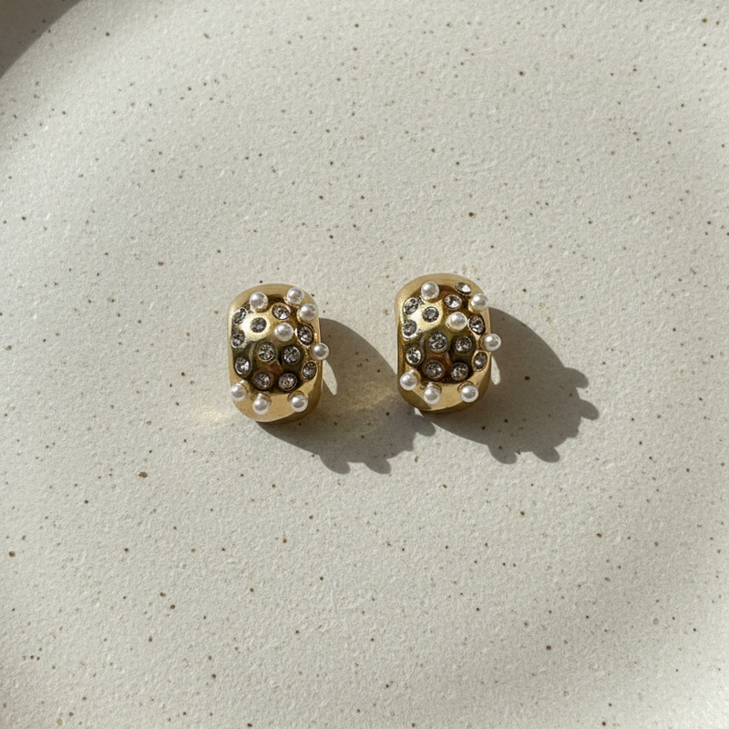 Gold huggie earrings with embedded white pearls and crystals on packaging.