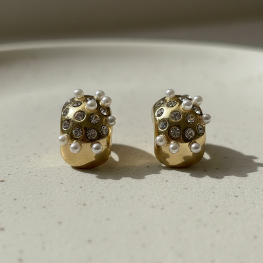 Gold huggie earrings with embedded white pearls and crystals on packaging.