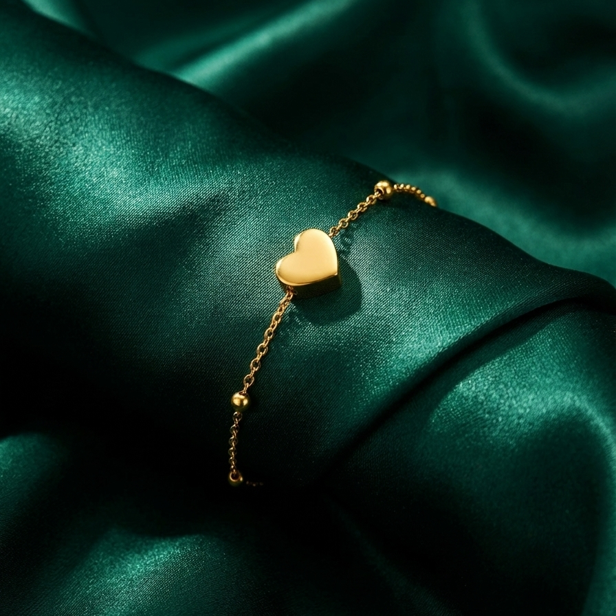 Dainty gold chain bracelet with small heart charm and beads on white stone background.