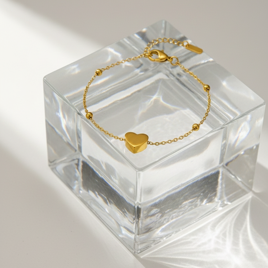 Dainty gold chain bracelet with small heart charm and beads on white stone background.