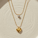 Double layered gold necklace with crystal solitaire and puffy heart pendant on beige plate.