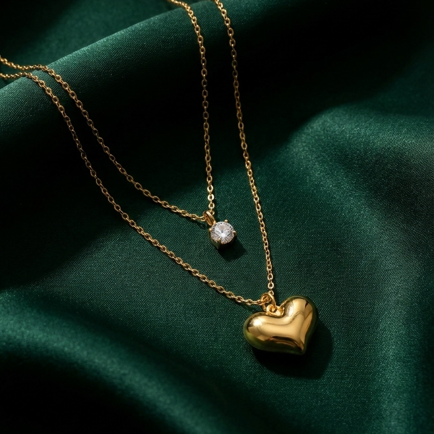 Double layered gold necklace with crystal solitaire and puffy heart pendant on beige plate.