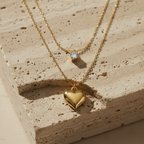 Double layered gold necklace with crystal solitaire and puffy heart pendant on beige plate.