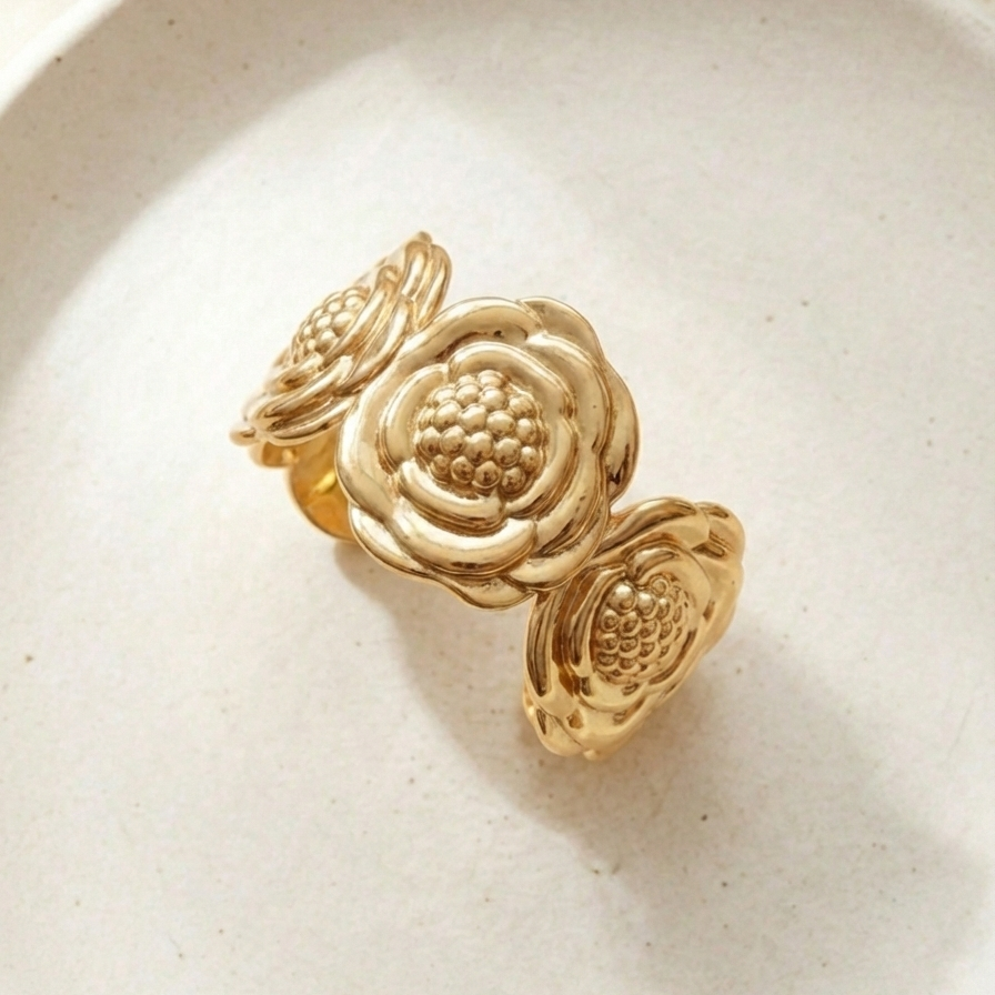 Wide gold cuff bracelet with sculpted camellia flower design on beige stone.