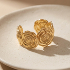 Wide gold cuff bracelet with sculpted camellia flower design on beige stone.