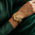 Wide gold cuff bracelet with sculpted camellia flower design on beige stone.