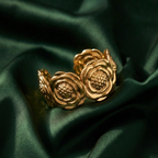 Wide gold cuff bracelet with sculpted camellia flower design on beige stone.