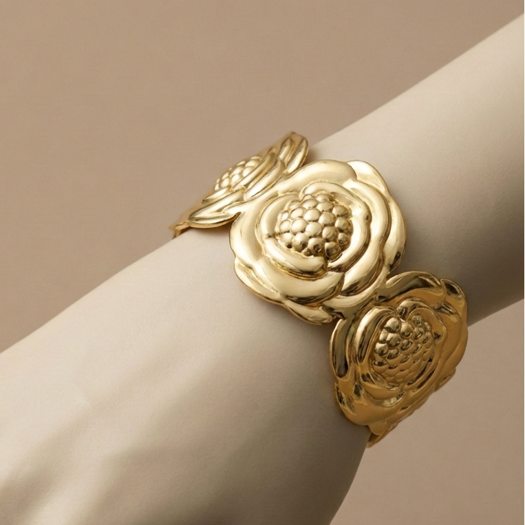 Wide gold cuff bracelet with sculpted camellia flower design on beige stone.
