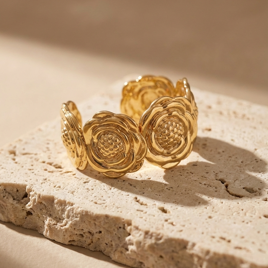 Wide gold cuff bracelet with sculpted camellia flower design on beige stone.
