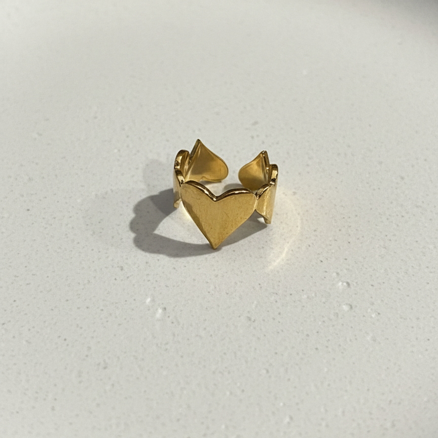 Gold heart shaped ring with crown details on beige background.