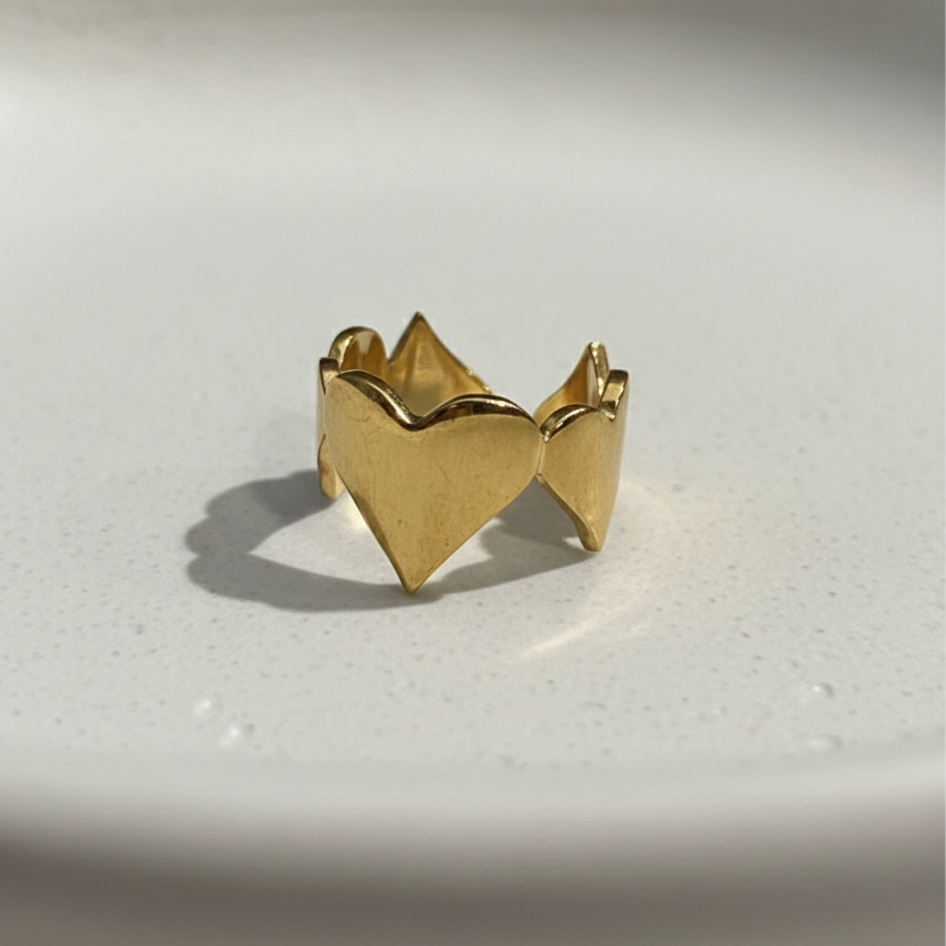 Gold heart shaped ring with crown details on beige background.