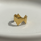 Gold heart shaped ring with crown details on beige background.