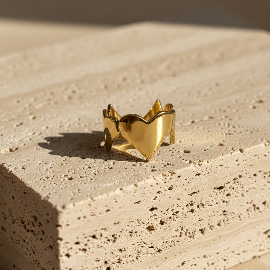 Gold heart shaped ring with crown details on beige background.