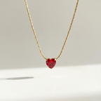 Gold necklace with faceted ruby red heart crystal pendant on white background.
