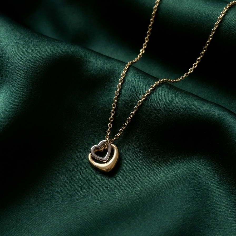 Gold necklace with a heart-shaped pendant on a dark green fabric background