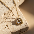 Gold necklace with a heart-shaped pendant on a textured stone surface