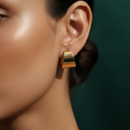 Wide sculpted gold huggie earrings on beige stone background.