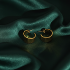 Wide sculpted gold huggie earrings on beige stone background.