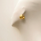 Wide sculpted gold huggie earrings on beige stone background.