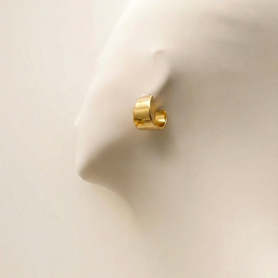 Wide sculpted gold huggie earrings on beige stone background.