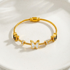 Gold cable wire bangle bracelet with black and white butterfly charms on white stone.