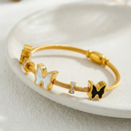 Gold cable wire bangle bracelet with black and white butterfly charms on white stone.