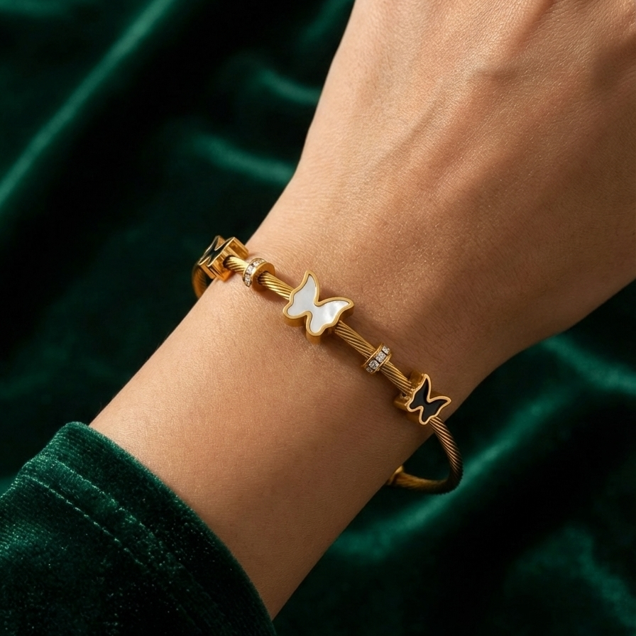 Gold cable wire bangle bracelet with black and white butterfly charms on white stone.