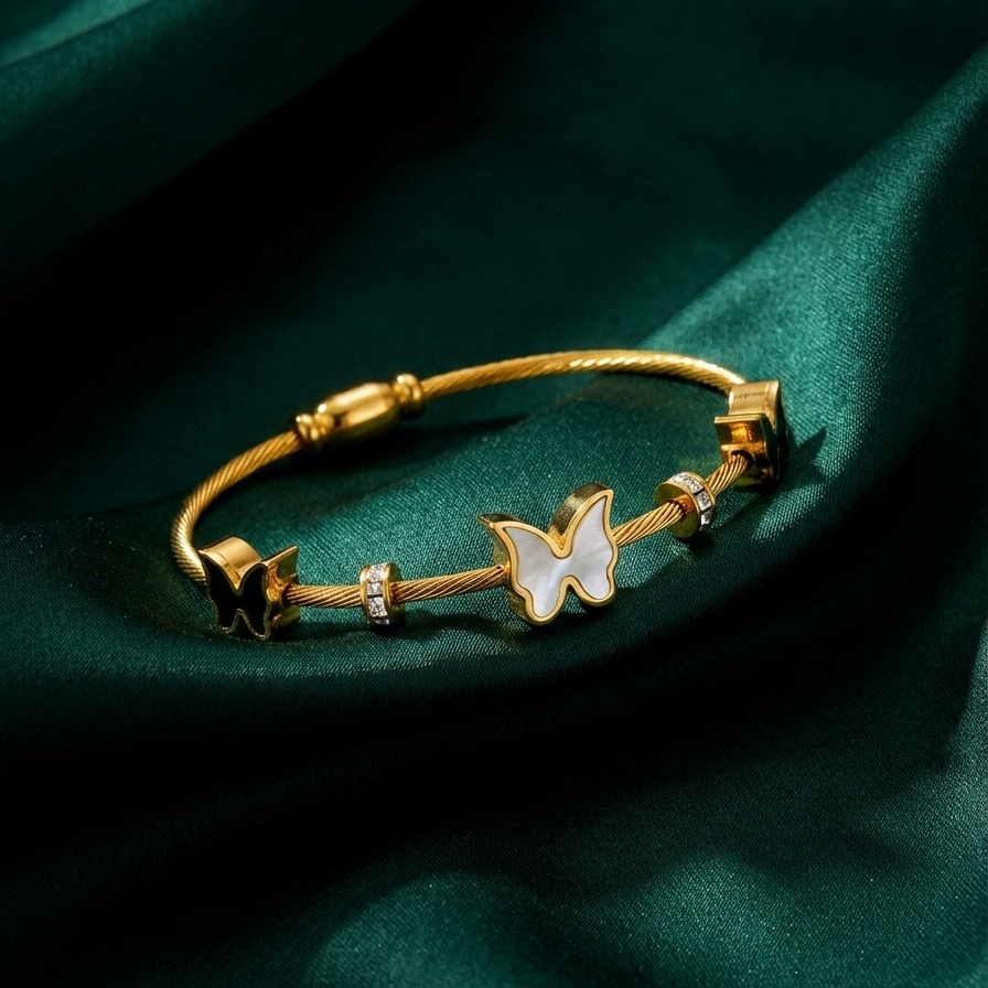 Gold cable wire bangle bracelet with black and white butterfly charms on white stone.