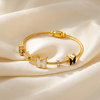 Gold cable wire bangle bracelet with black and white butterfly charms on white stone.
