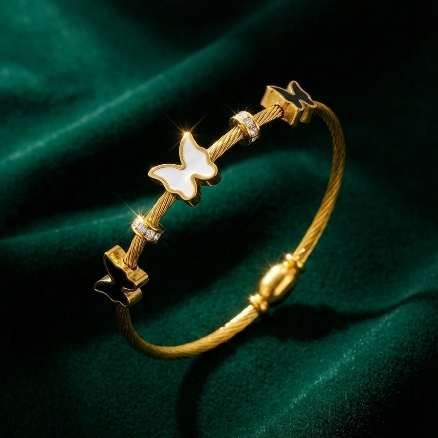 Gold cable wire bangle bracelet with black and white butterfly charms on white stone.