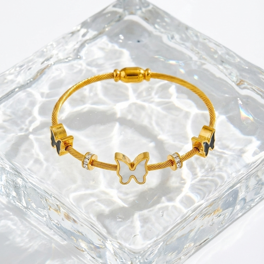 Gold cable wire bangle bracelet with black and white butterfly charms on white stone.
