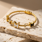 Gold cable wire bangle bracelet with black and white butterfly charms on white stone.