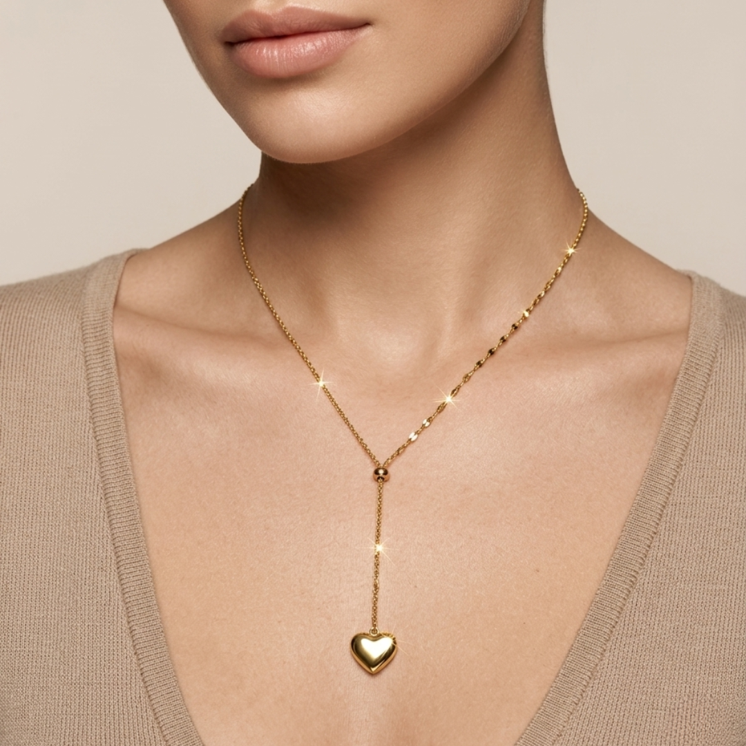 Woman wearing a 18kt gold plated necklace with a heart shaped pendant against a neutral background.
