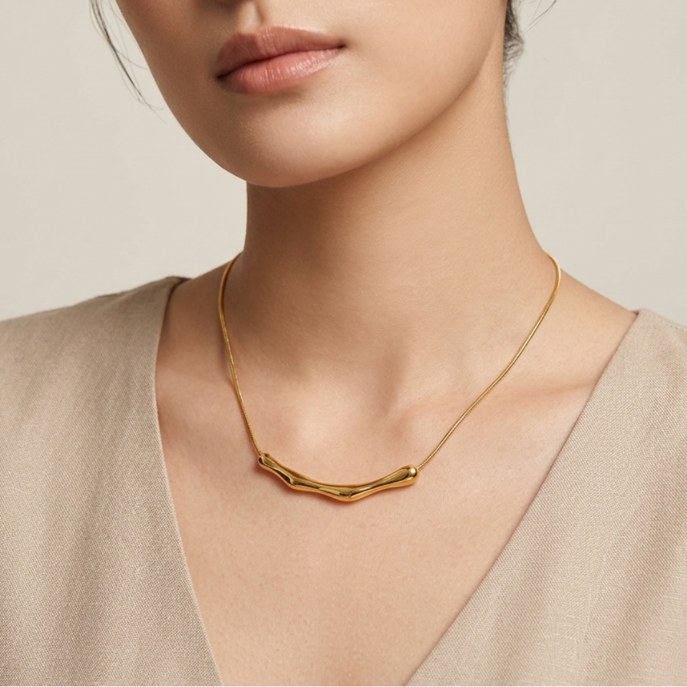 Woman wearing a 18kt gold plated bamboo bar necklace against a neutral background.